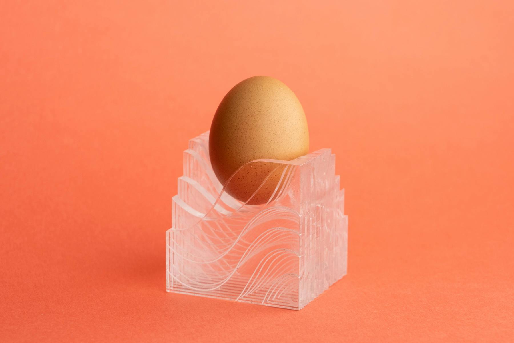 EggHolder 9, an incomplete cube made of stacked acrylic pieces, holding an egg against a salmon-colored background.