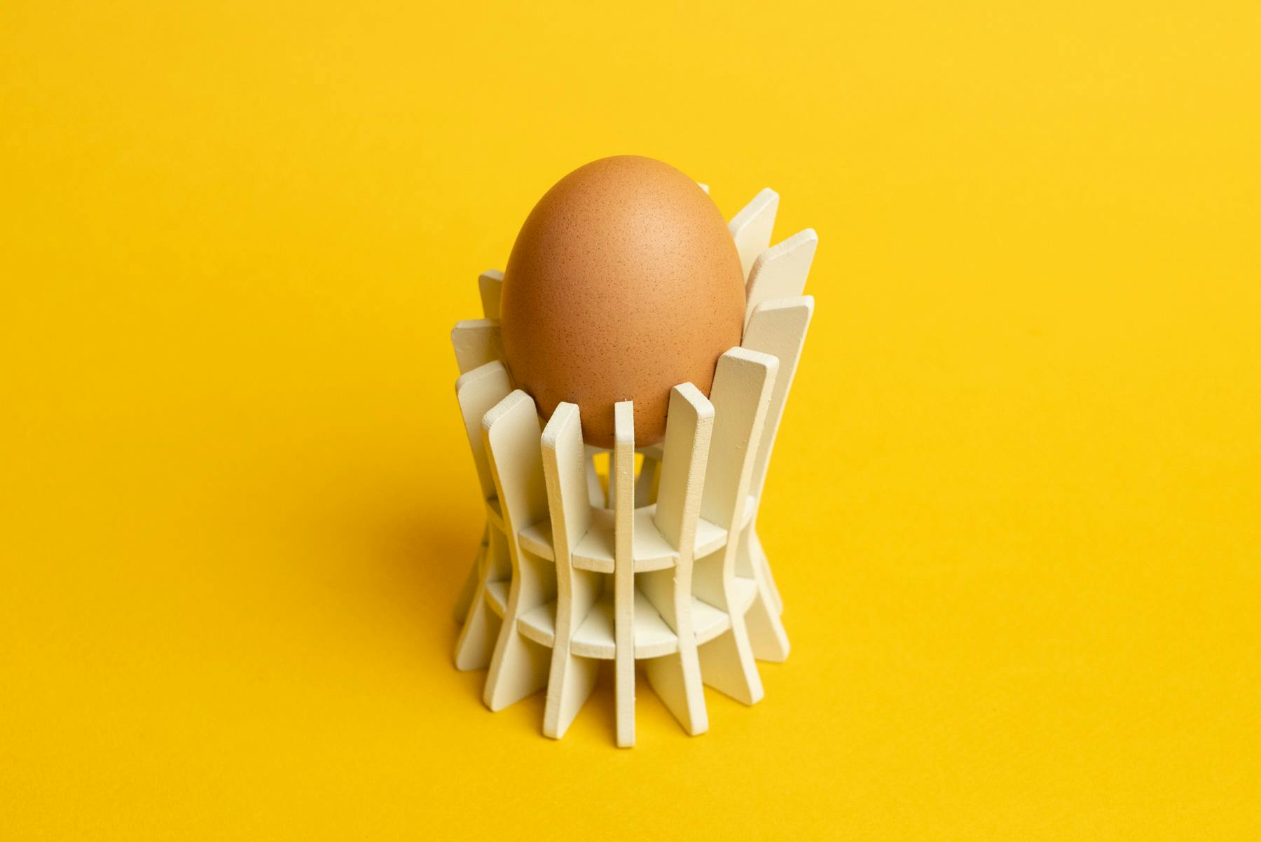EggHolder 1, a white cylindrical fin loft model, holding up an egg against a bright yellow background.
