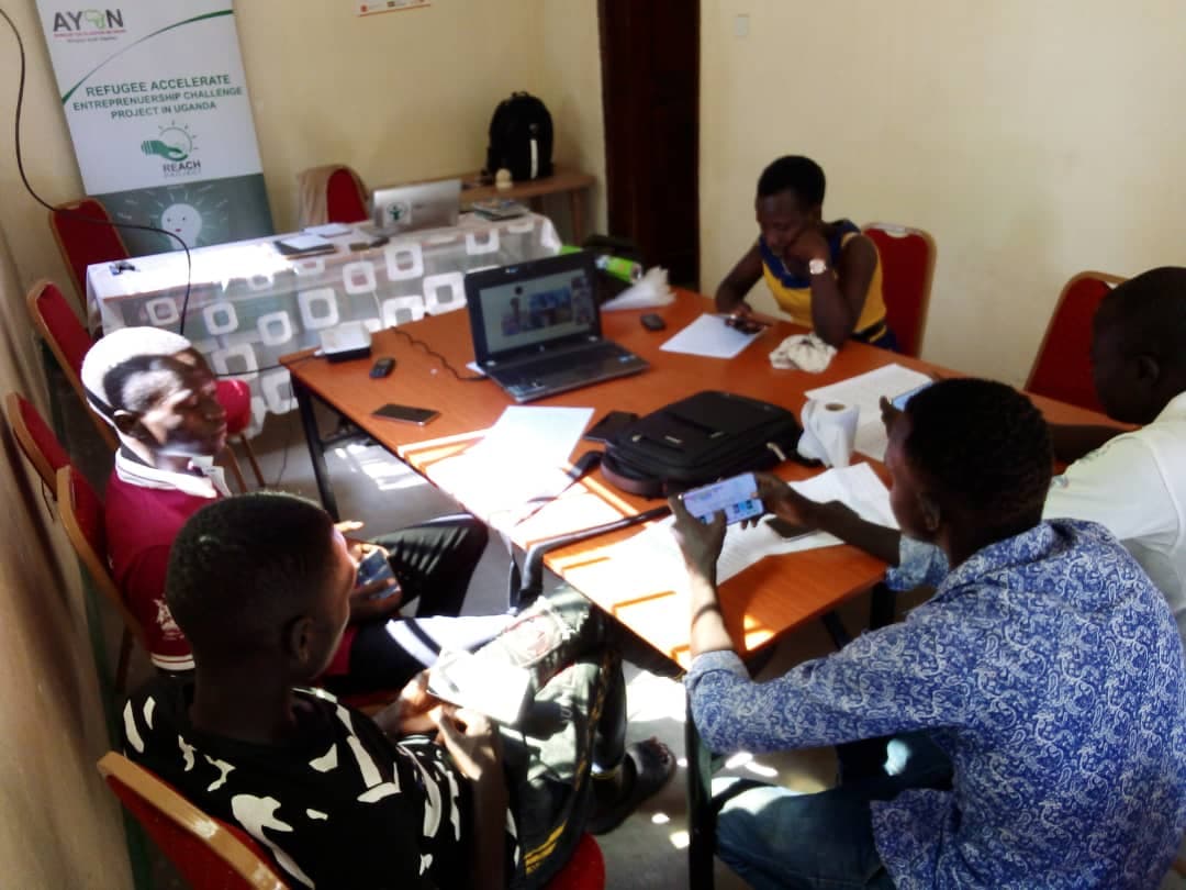 Five Ugandan refugees playing with Mini Synth around a table. Slides with teaching materials can be on the laptop in the middle of the table.