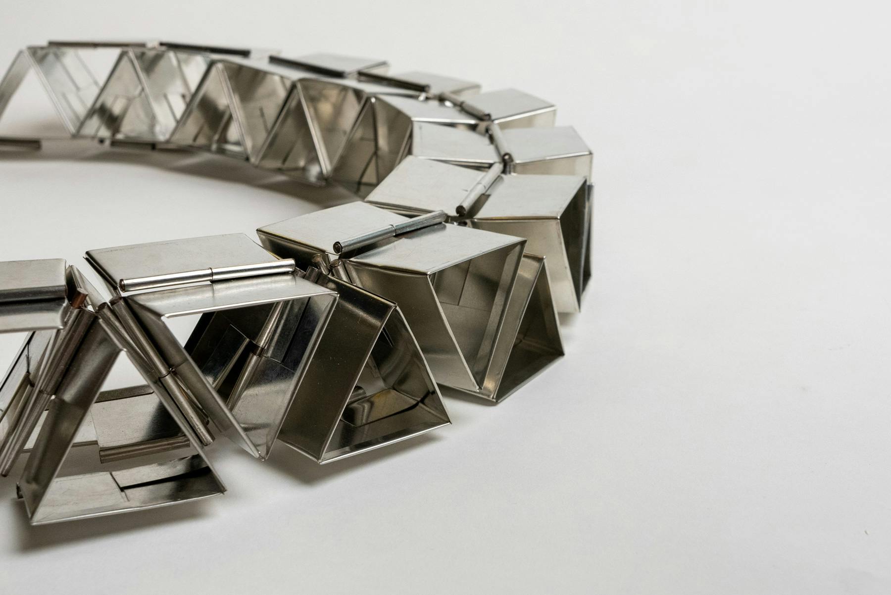 A long sequence of modular triangular prisms made from tin sheets attached using hinges. These hinges allow for fluid movement in an otherwise solid object.