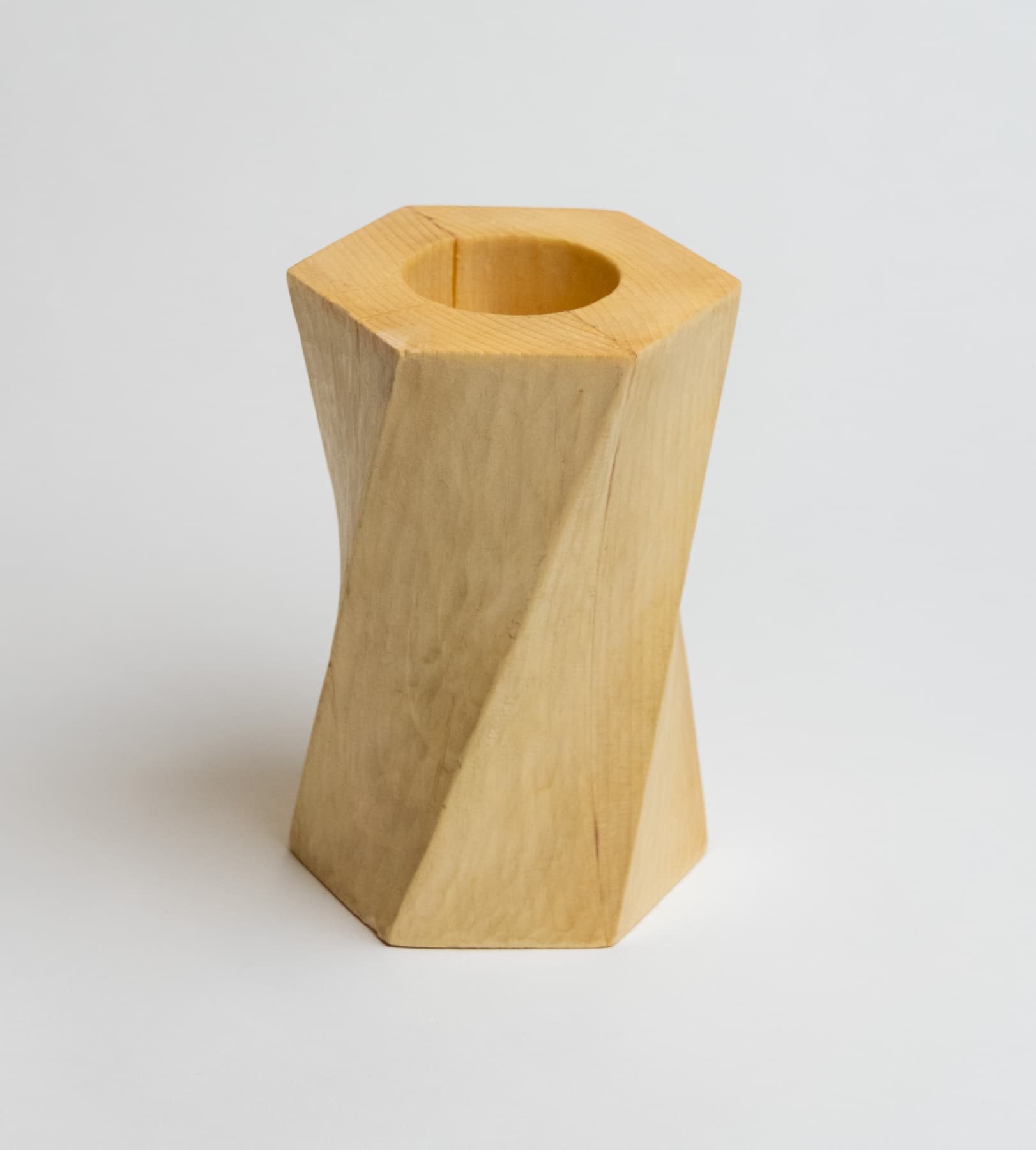 A twisted hexagonal prism made of pine wood with a deep cavity at the top.